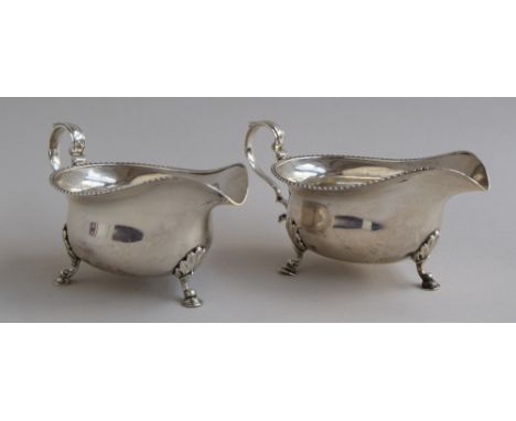 A matching pair of Edwardian silver Mappin & Webb gravy boats on paw feet with scallop shell finials and a scrolled handle, S