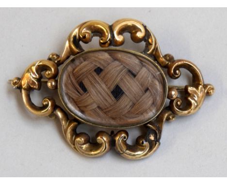 A Victorian gold mourning brooch, circa 1840, containing a lock of hair surrounded by a scrolled border in gold