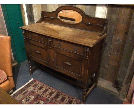 Antique sideboard buffet in Jacobean revival taste. Dark stained oak, brass pulls. Oval mirror plate with bevelled edge and l