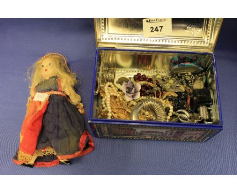 Tin containing assorted costume and dress jewellery, brooches, beads together with vintage small doll in dress with painted f