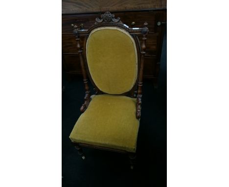 A walnut framed bedroom chair with gold fabric upholstered seat and back rest, resting on turned supports to ceramic castors.