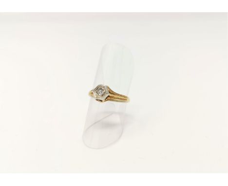 A yellow and white metal solitaire ring with diamond in hexagonal setting, relief decoration to the shoulders 