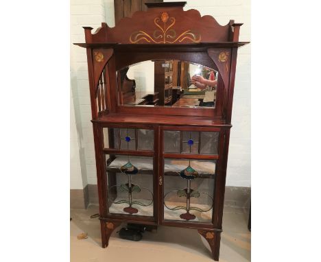 An Art Nouveau inlaid mahogany display cabinet with mirror back, open shelf with side spindles over twin coloured leaded door