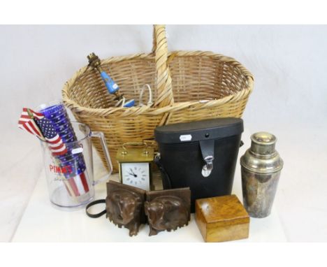 A wicker basket containing a mixed lot of collectables to include binoculars, cocktail shaker and a lamp base.
