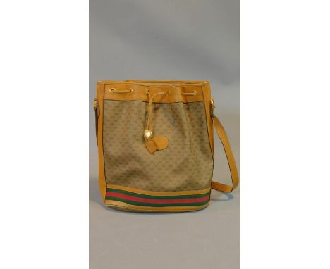 A vintage 80's tan leather and Gucci Canvas drawstring bucket bag with red and green striped strapping around the bottom. Wit