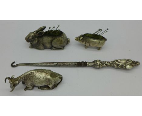 A silver handled button hook, two silver pin cushions in the form of a pig and a rabbit and a silver cow