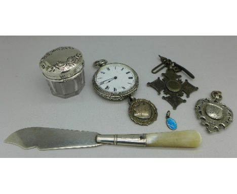 A silver fob watch, three silver fobs, a silver topped jar, a silver butter knife and a charm