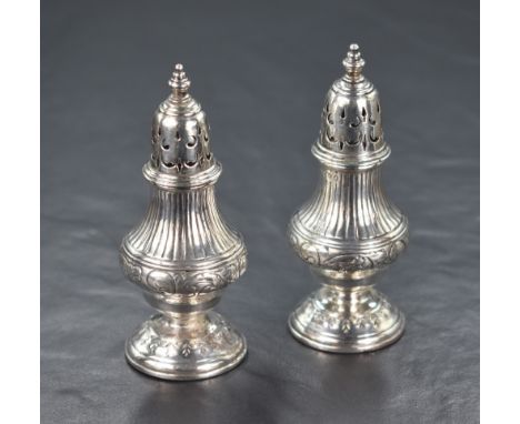 A pair of Victorian silver pepperettes, of bulbous form having decorative line work and scroll engraving, raised on an engrav