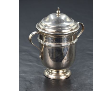 A George V silver cup and cover, of traditional form having a step moulded cover with finial, C-curve handles to the sides wi