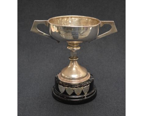 A George V silver trophy cup, of traditional for having angular handles, raised on a knopped stem with a circular step moulde