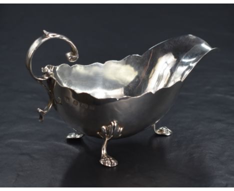 An early George V silver sauce boat, with Chippendale style rim, narrow spout opposed by a scrolling handle, raised on three 