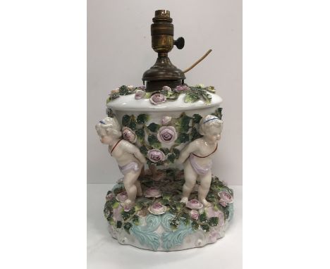 A late 19th Century Schierholz oil lamp as four putti holding aloft a rose encrusted bowl and cover on a similarly decorated 