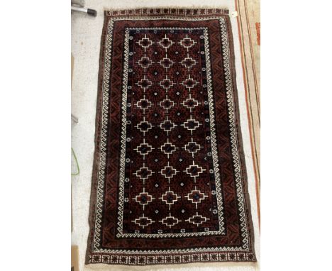 A Belouch tribal rug, the central panel set with repeating stylised tarantula motif design on a dark plum ground within a ste