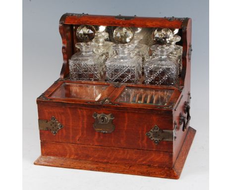 A late Victorian oak and silver plate mounted three bottle tantalus, having inset mirror with twin bevelled glass hinged cove