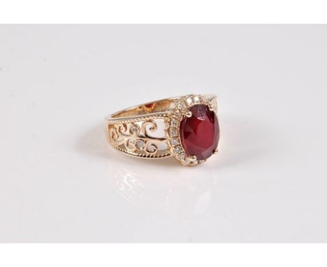 A 14k treated ruby and diamond ring, the oval claw mounted ruby, surrounded by small round diamonds, with tapered filigree sh