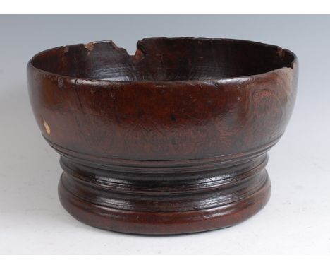 A turned elm bowl, of good size, raised on four small pad feet, probably first half 18th century, dia.39cm. With losses. One 