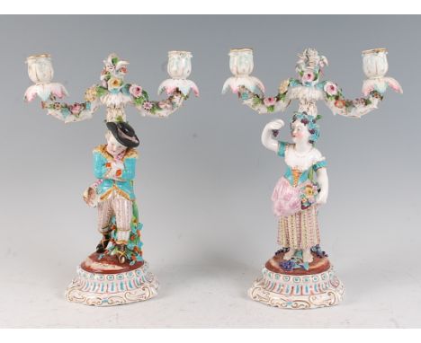 A pair of continental porcelain two-light candelabra, modelled as a young huntsman and his maiden holding aloft a bunch of gr
