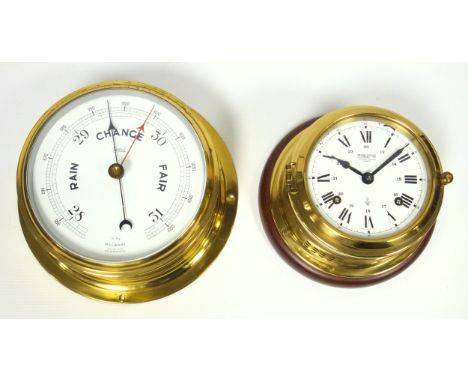 Wempe marine chronometer with a white circular dial enclosing a mechanical movement, in a brass circular case, on a mahogany 