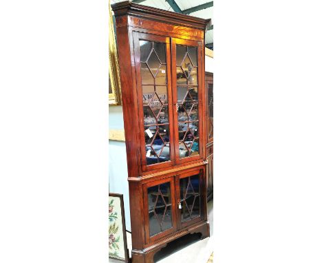 A Georgian mahogany floor standing corner cabinet with moulded cornice and inlaid frieze, enclosed by two pairs of astragal g