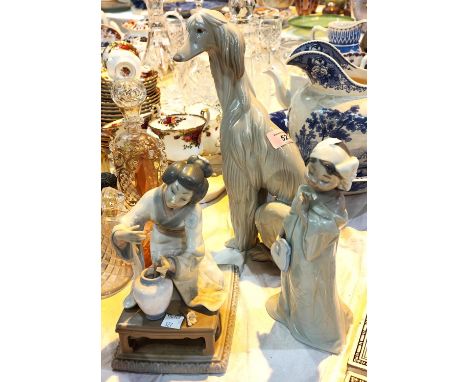 A Lladro figure of a dog, height 30cm; a Lladro figure of a Japanese girl flower arranging (flowers missing) and a Nao figure