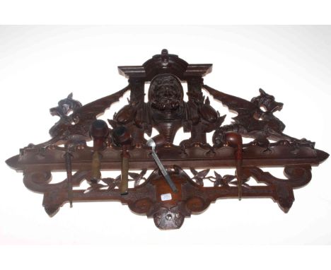 Heavily carved mahogany pipe rack with pipes.