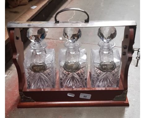 A three bottle mahogany tantalus with cut glass decanters &amp; hallmarked silver labels for whiskey, brandy and gin, complet