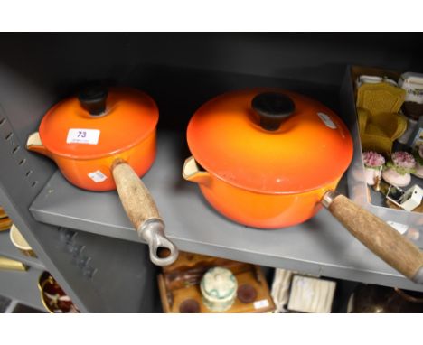 Two modern Le Creuset lidded sauce pans in orange enamel.