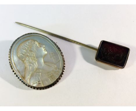 A carved mother of pearl cameo of a young girl and a carved black stone stick pin