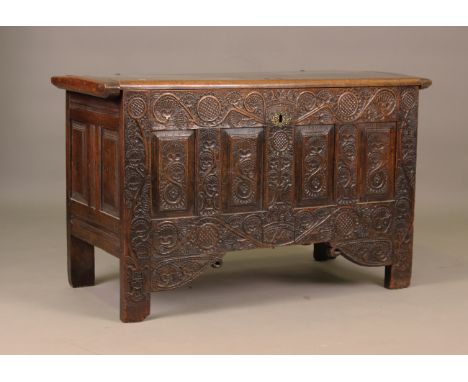 A 17th century oak panelled coffer, the hinged lid enclosing two candle boxes, the four panel front finely carved with styliz