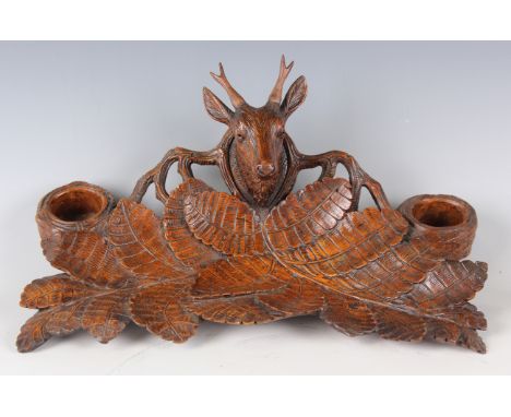 A late 19th century Black Forest carved wooden desk stand, the central stag head surmount flanked by twin inkwell recesses, o