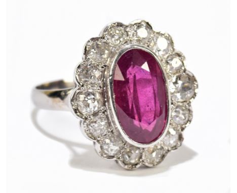 An 18ct white gold diamond and ruby cluster ring, the central oval ruby set within a border of sixteen old cut diamonds, size