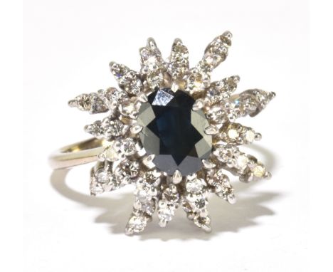 An 18ct white gold sapphire and diamond stepped ring with central dark blue/black oval sapphire within a border of round bril