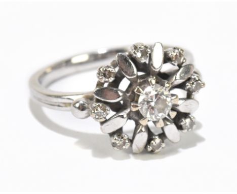 A white metal diamond set floral dress ring, the central diamond flanked by a melee of eight diamonds,&nbsp;approximate size 