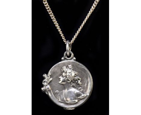 A French Art Nouveau white metal circular pendant decorated with the profile portrait of a young woman and indistinctly signe