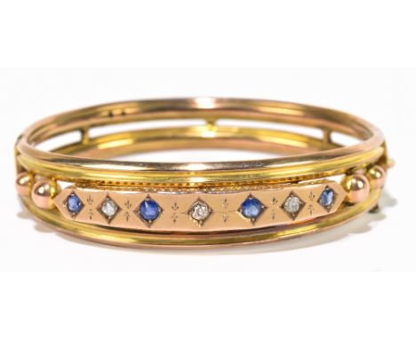 An Edwardian yellow metal diamond and sapphire oval hinged snap bangle, the central platform set with four sapphires and thre