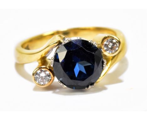 An 18ct yellow metal sapphire and diamond three stone ring, the circular sapphire flanked by collet set diamonds, in swept mo