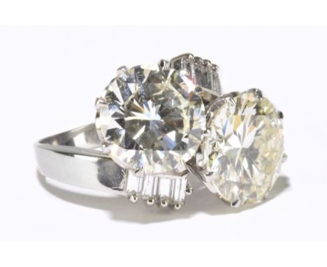 A white metal diamond crossover ring with twin round brilliant cut stones weighing 4.20ct and 3.66ct, with eight further bagu