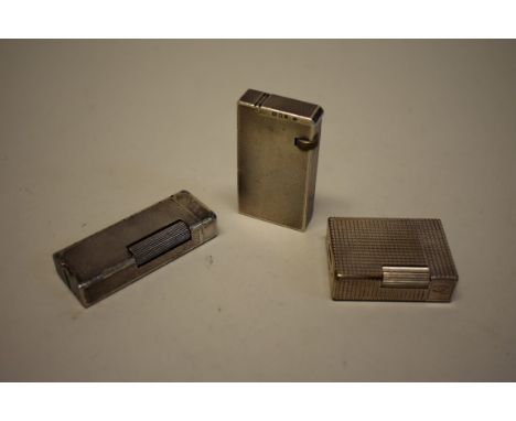 A Dunhill silver engine turned lighter, London 1935; together with a silver plated Dunhill example; and another by ST Dupont.