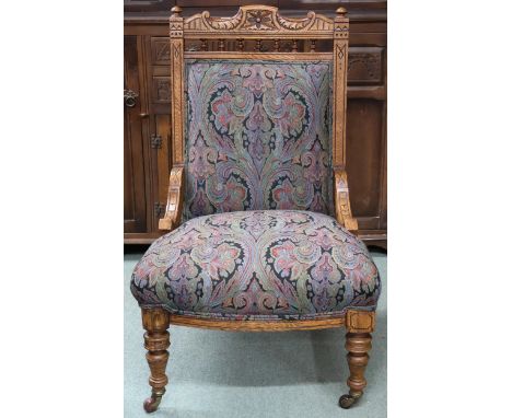 A Victorian oak framed nursing chair with damask upholstery on turned supports terminating in ceramic casters, 99cm high x 65
