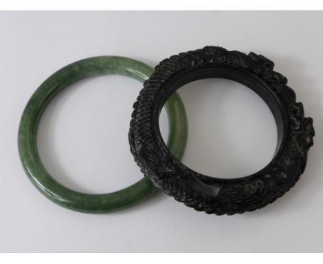 A Chinese Black Hard Stone Bangle, depicting chasing dragons and flaming pearls of wisdom together with a green hard stone ba
