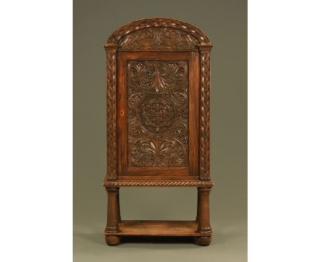 A late 19th/early 20th century carved oak cupboard, with arched pediment, carved door with turned supports and shelf beneath.