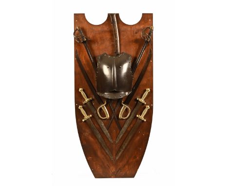 A collection of weaponry displayed on a large shield shaped backboard, to include a breastplate, swords, cutlasses and other 