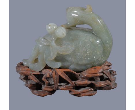 A Chinese jade or jadeite figure of a Phoenix, holding a peach branch, the jadeite 10.5cm wide x 7.2cm high, carved wood stan