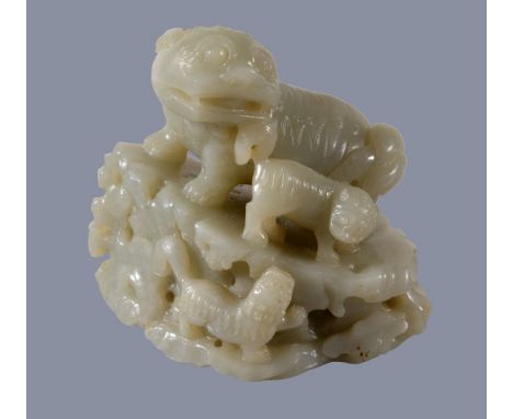 A Chinese celadon jade carving of a Buddhist 'lion and cubs', standing on a pierced and openwork rock, looking back towards t
