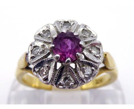 A ruby and diamond cluster ring, the circular cluster centred on a small round cut ruby, in a segmented surround of illusion 