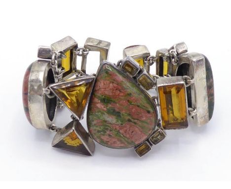 A unakite and paste set bangle, the large geometric pattern of stones mounted in silver, 20cm long CONDITION: one stone missi