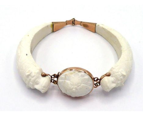 A 19th century carved white coral bangle, composed of two hinged sections terminating in a bear's head, a foliate boss betwee
