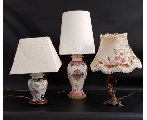 THREE TABLE LAMPSone raised on an hexagonal base with a porcelain body decorated with flowers, with a cream shade, 53cm high,