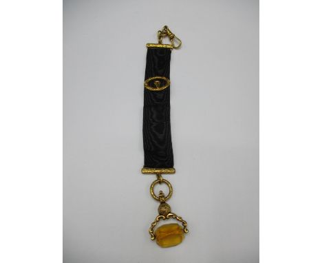 A 19th century gold coloured metal and black fabric fob with a clasp, chain, engraved ends and buckle style ornament and a ro