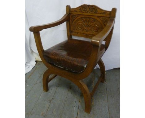 An Elizabethan style light oak armchair with carved scroll and leaf back and leather seat